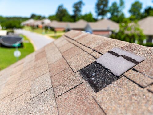 Damaged roof shingles with a patch of snow on a suburban house rooftop