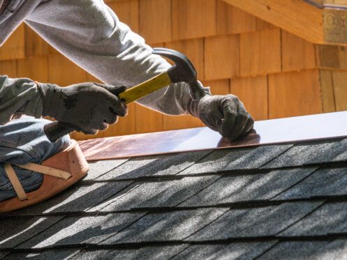 Worker hammering roofing shingles on a house roof