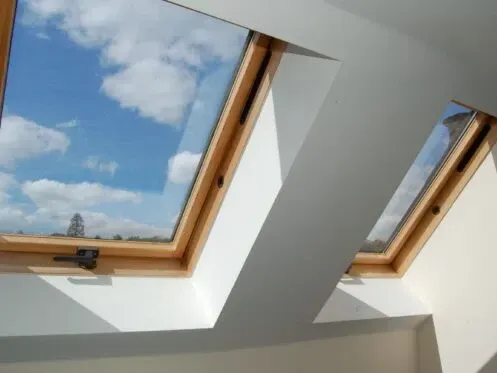 Two skylights in a white ceiling showing blue sky and clouds