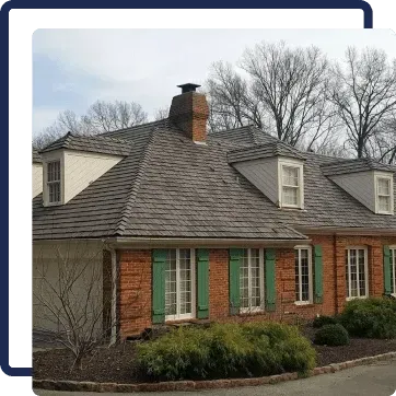 Brick house with gray shingled roof, green shutters, and dormer windows behind leafless trees