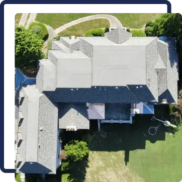 Aerial view of a large house with gray roof, driveway, and green lawn.
