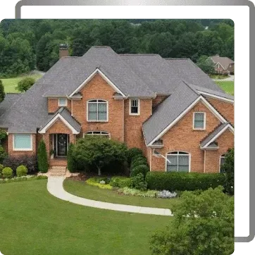 Large brick suburban house with gray roof, white trim, and a curved front walkway surrounded by green lawn.