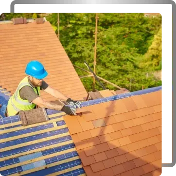 Worker in blue hard hat installing shingles on a steep roof outdoors
