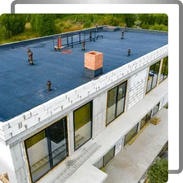 Flat-roof building under construction with blue waterproofing, rooftop vents, and exposed windows.