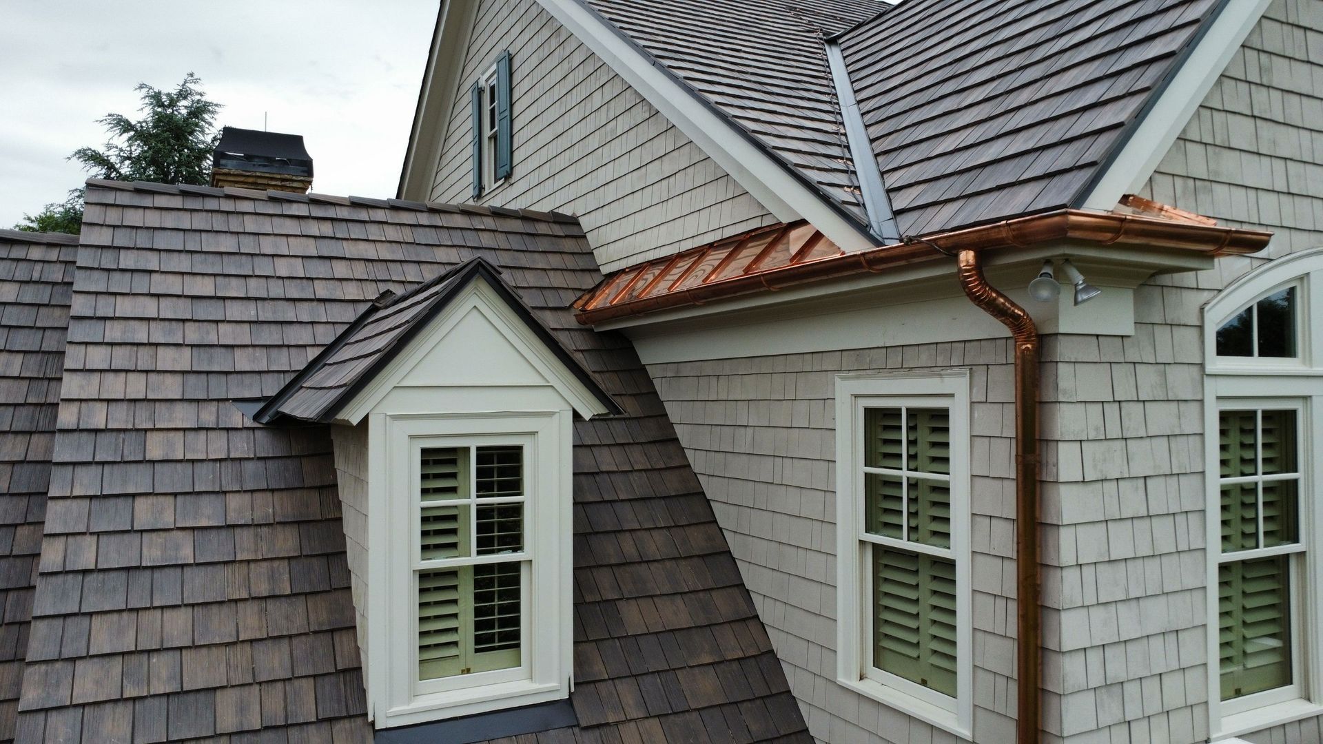 Close-up of a house roof with white gutters and downspout against a blue sky