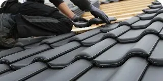 Worker installing dark gray roof tiles on a roof slope