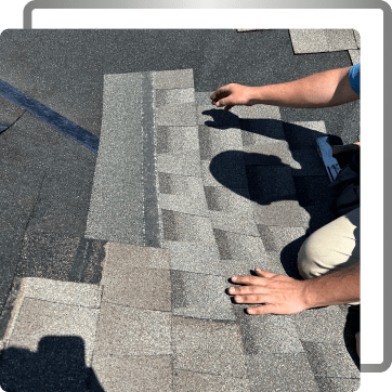 Worker installing gray roof shingles on a sloped roof, aligning replacement pieces by hand