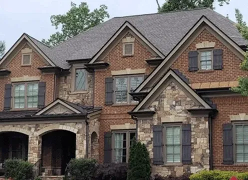 Large two-story brick house with stone accents, arched entryways, and a dark shingled roof
