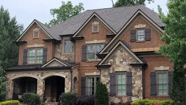 Large brick suburban house with stone accents, arched garage, and manicured greenery