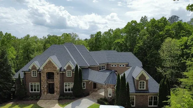 Large brick house with solar panels on the roof, surrounded by trees under a cloudy sky