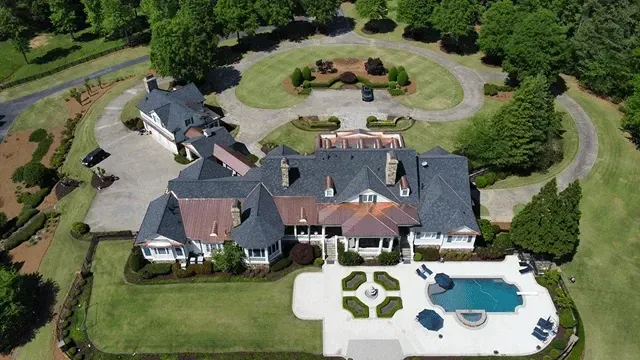 Aerial view of a large house with a landscaped lawn, circular driveway, and backyard swimming pool