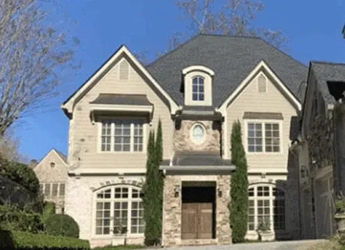 Large beige stone house with arched windows, tall peaked roof, and front entry under a bright blue sky