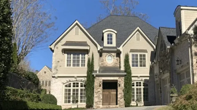 Large stone house with steep gray roof, ivy-covered entry, and tall windows on a sunny day