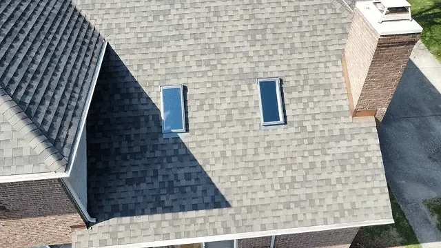 Aerial view of a gray shingled roof with two skylights and a brick chimney.