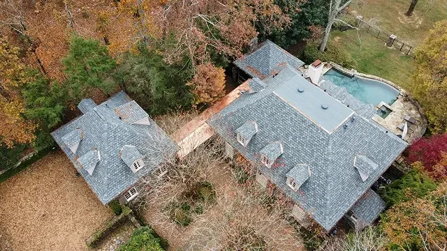 Aerial view of two gray-roofed houses surrounded by autumn trees and a backyard pool