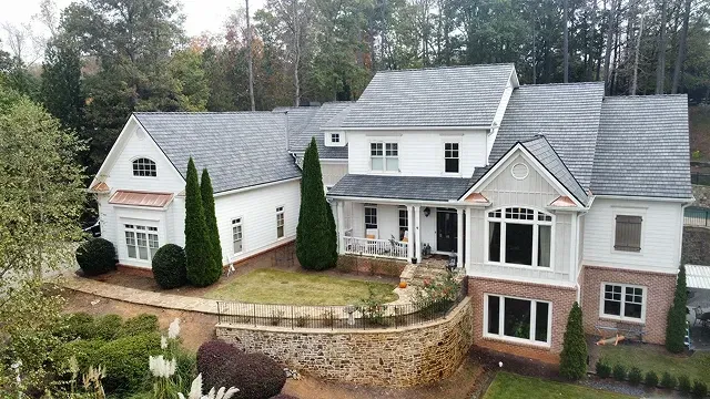 Large white suburban house with gray roof, stone accents, and a landscaped front yard amid trees.