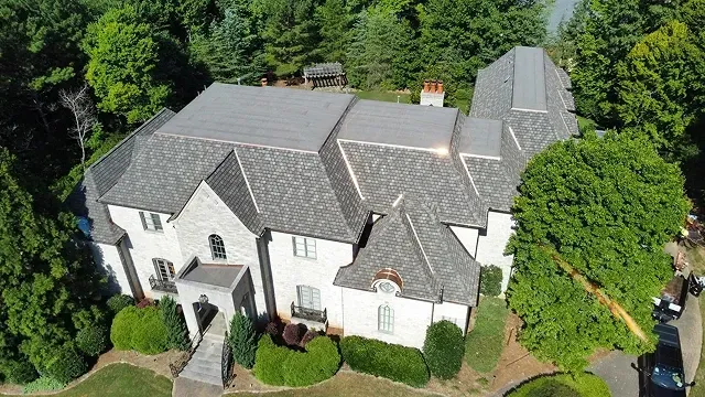 Aerial view of a large white house with gray roof, surrounded by trees and landscaped yard