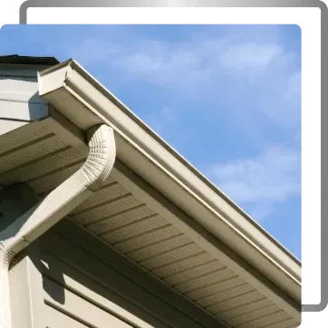 Close-up of a house roof with white gutters and downspout against a blue sky