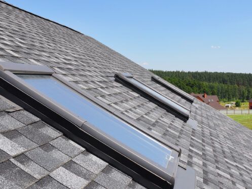 Grey shingled roof with two skylights under a clear blue sky