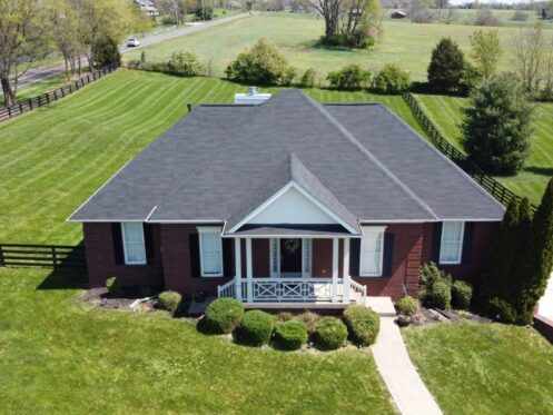 Aerial view of a brick house with a gray roof, front porch, and large green lawn.
