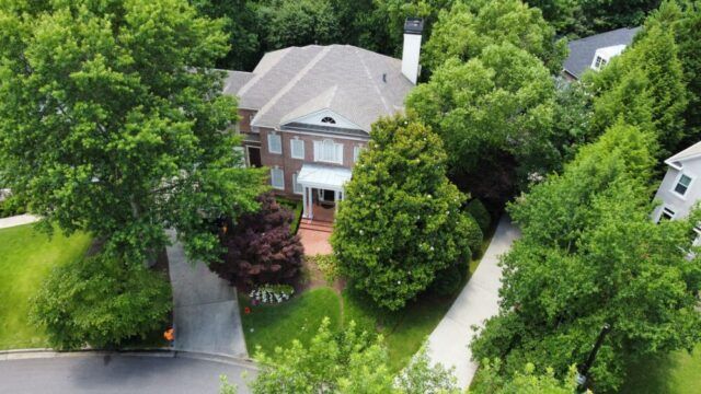 Aerial view of a house surrounded by dense green trees and a curved driveway