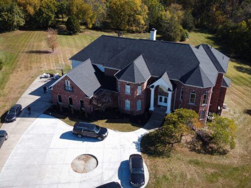 Aerial view of a large brick suburban house with a circular driveway and cars parked outside