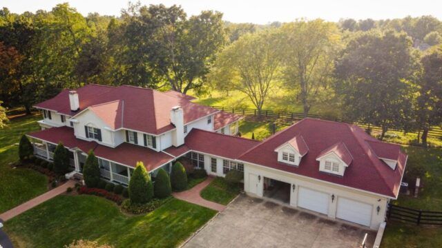 Aerial view of a large white house with a red roof, attached garage, and trees surrounding it.