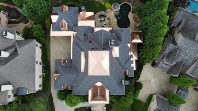 Aerial view of a large gray-roofed house with a central courtyard and surrounding trees