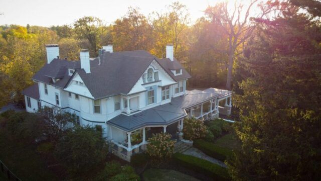 White Victorian house with a wraparound porch surrounded by trees at sunset