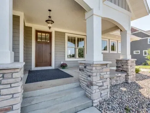 Front porch of a modern house with stone columns, steps, and a wooden front door