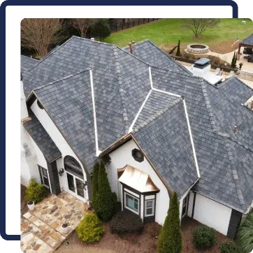 Aerial view of a house with a gray shingle roof, stone entry, and landscaped front yard.