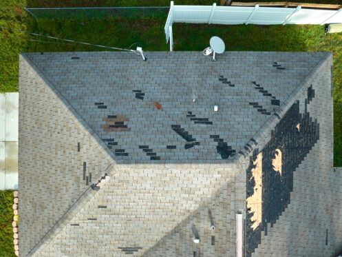 Aerial view of a house roof with dark shingles, visible wear, and a white satellite dish.