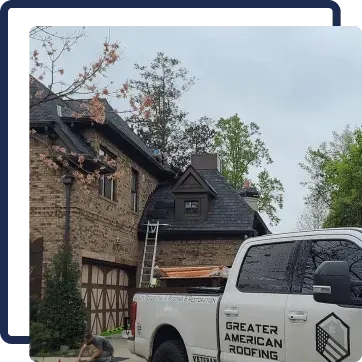 White pickup truck parked by a stone house with a ladder leaning to a dark roof amid trees
