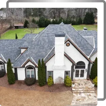 Aerial view of a white house with gray roof, tall chimney, arched windows, and a stone driveway.