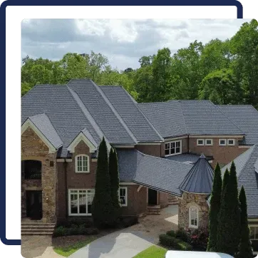 Large brick house with dark gray roof and tall evergreens, surrounded by trees under a cloudy sky