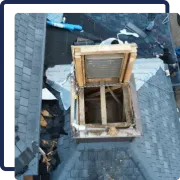 Damaged rooftop with open attic hatch and debris on gray shingles