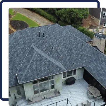 Aerial view of a house with a gray shingled roof and light patio decking below.