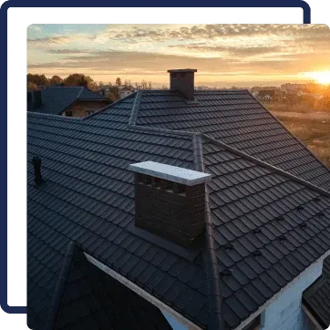 Rooftop with dark gray tiles and brick chimneys at sunset, with a cloudy orange sky.