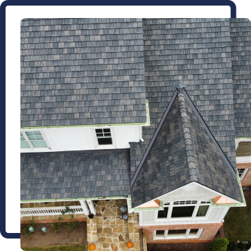 Aerial view of a house roof with gray shingles, dormer windows, and a stone entryway.