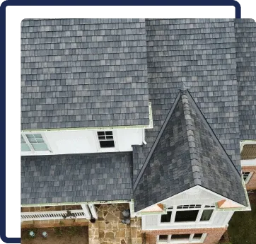 Aerial view of a gray shingled roof with dormer windows and a stone chimney.