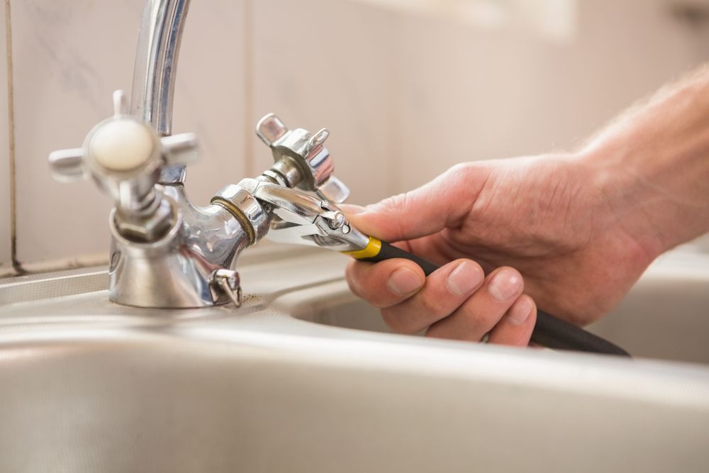 Person Using a Wrench to Repair a Faucet in a Kitchen Sink — Stewys in Tweed Heads, NSW