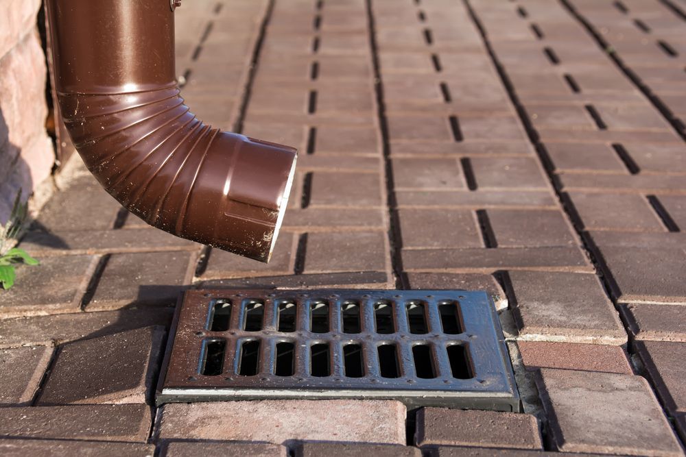 Brown Downspout Emptying Water Into a Metal Drain Set in Brick Paving — Stewys in Casuarina, NSW