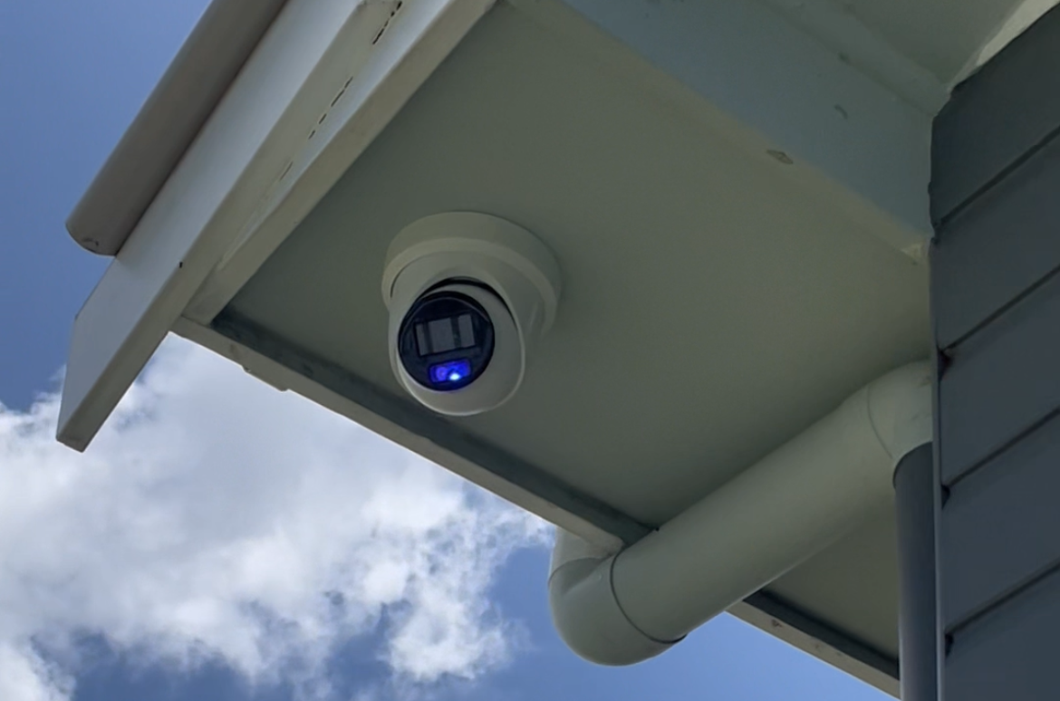 Outdoor security camera mounted under a house eave with a blue indicator light