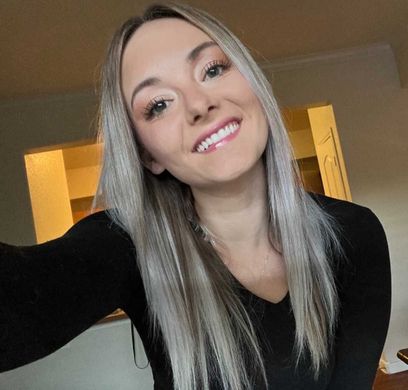 A woman in a black shirt is smiling and taking a selfie.