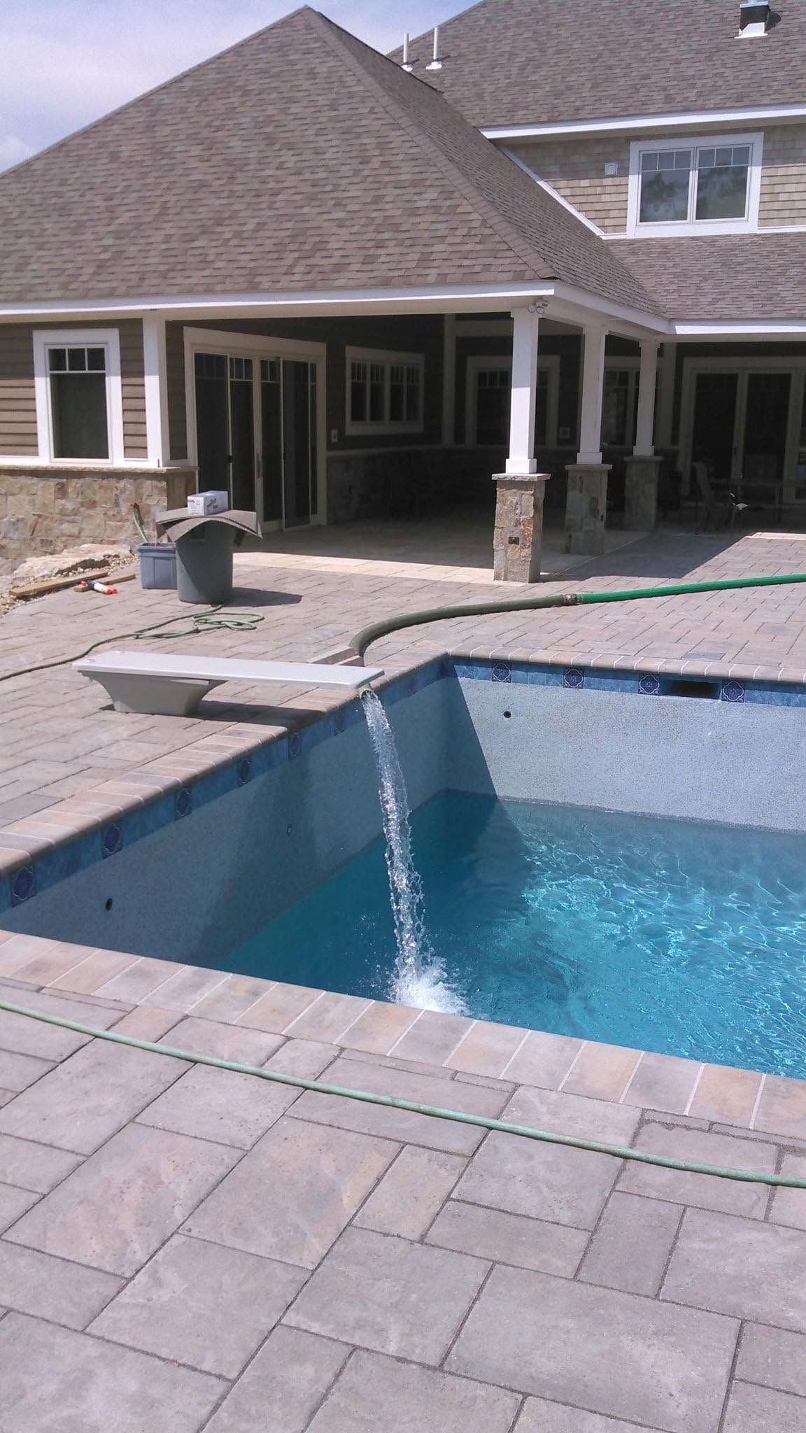 Backyard pool with stone patio and covered seating area beside a house