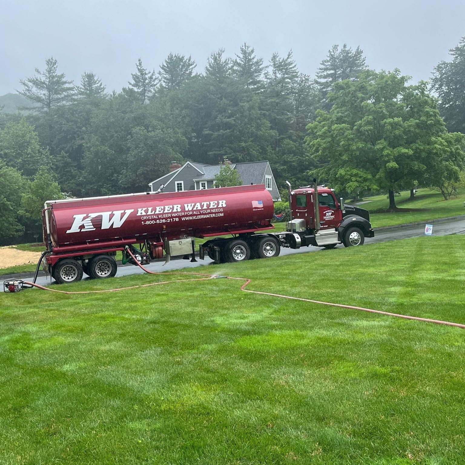 Red tanker truck parked on a wet grassy field near trees in light fog Red tanker truck parked on a wet grassy field near trees in light fog