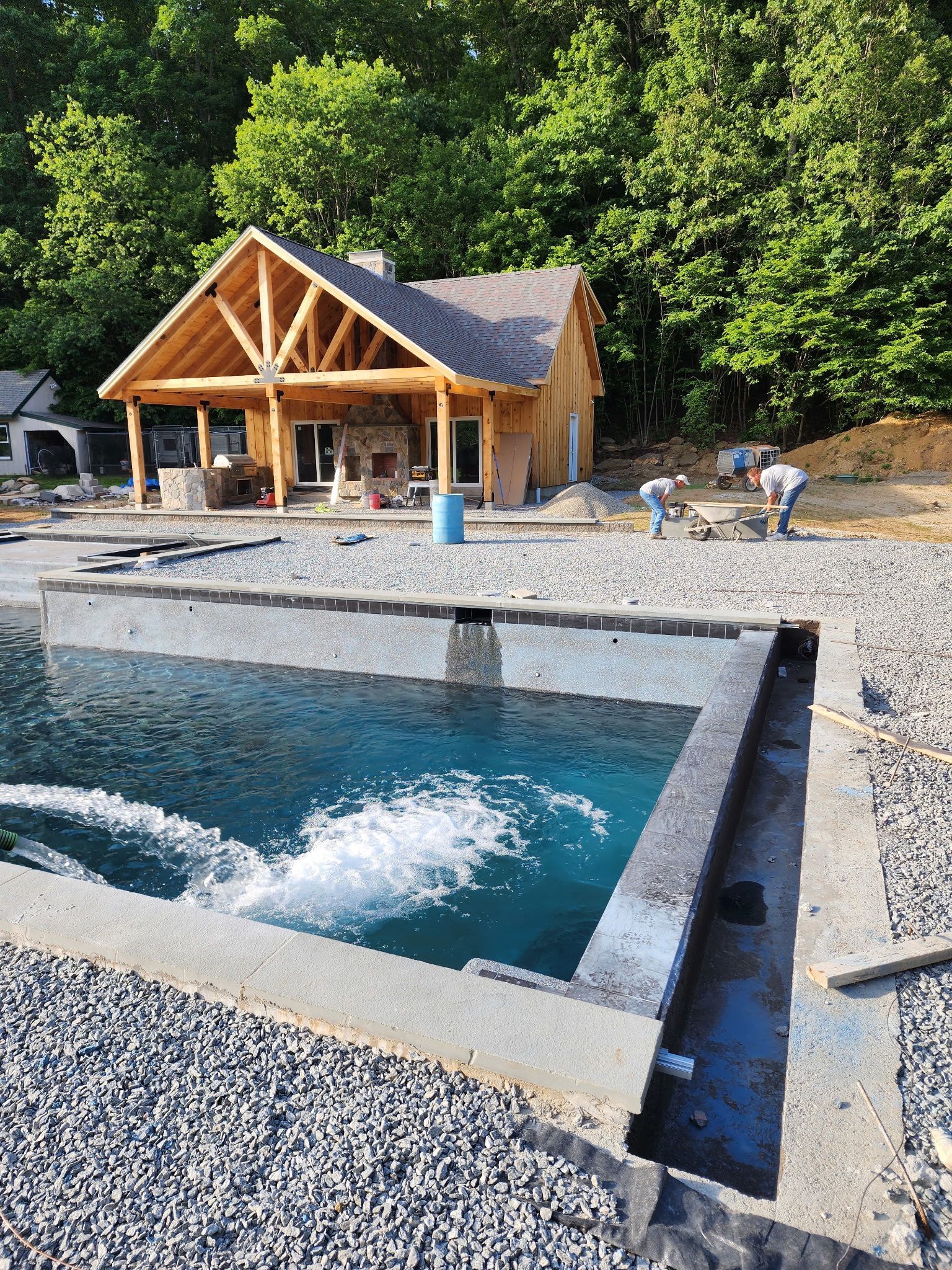 Stone pool splashing in front of a wooden cabin at the edge of a forest