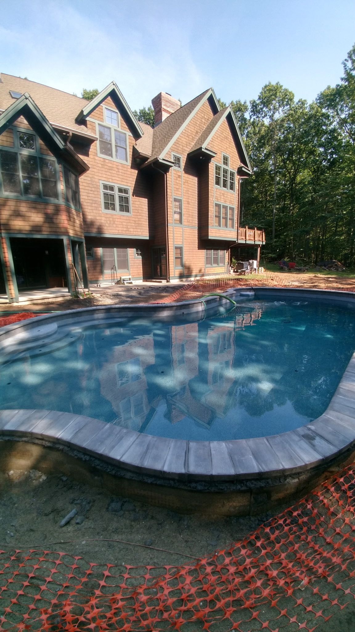 Brick house with a blue swimming pool and wooded backyard in bright daylight