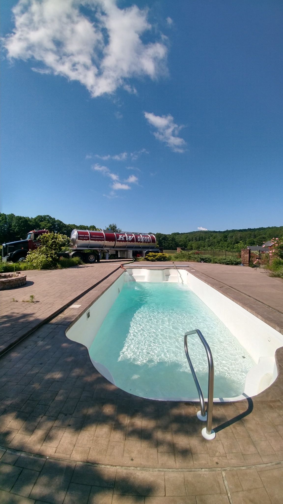 Outdoor swimming pool with clear blue water, concrete deck, and lounge chairs under a bright sky.