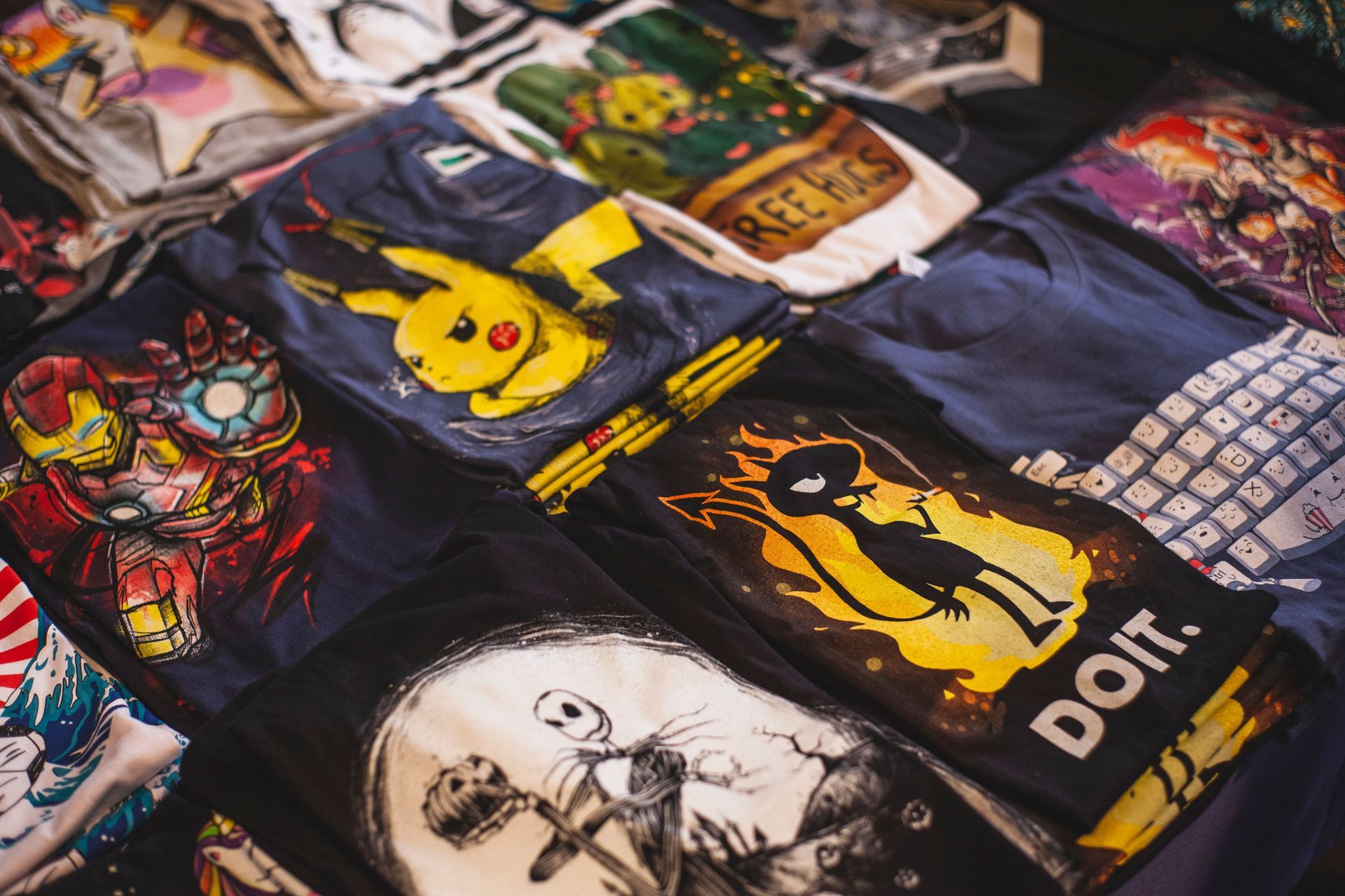 Assorted graphic T-shirts laid out on a table, featuring colorful pop-art and anime-style prints.